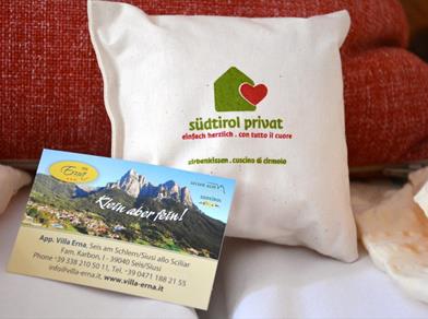 Zirbenkissen mit „südtirol privat“-Logo und Visitenkarte der Villa Erna vor rotem Polster.