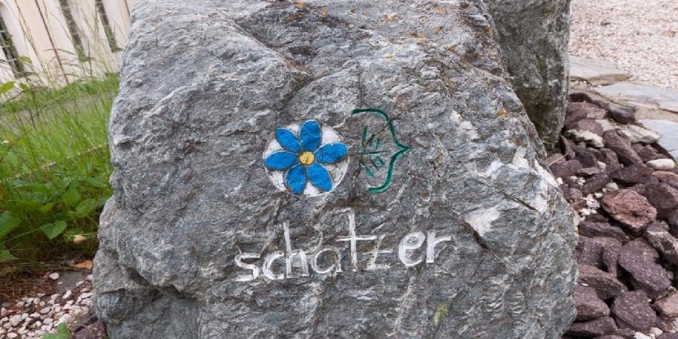 Grande pietra grigia con un fiore blu dipinto e la scritta “schatzer”